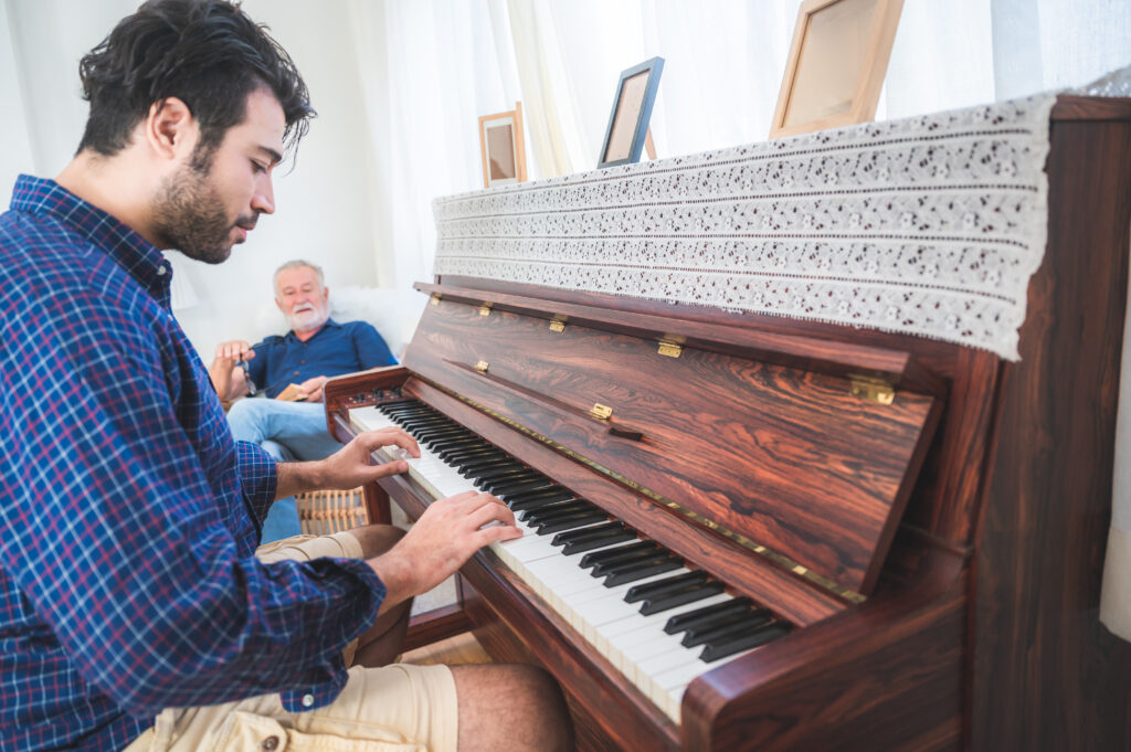 Un jeune homme joue du piano et un vieil homme assis à côté l'écoute