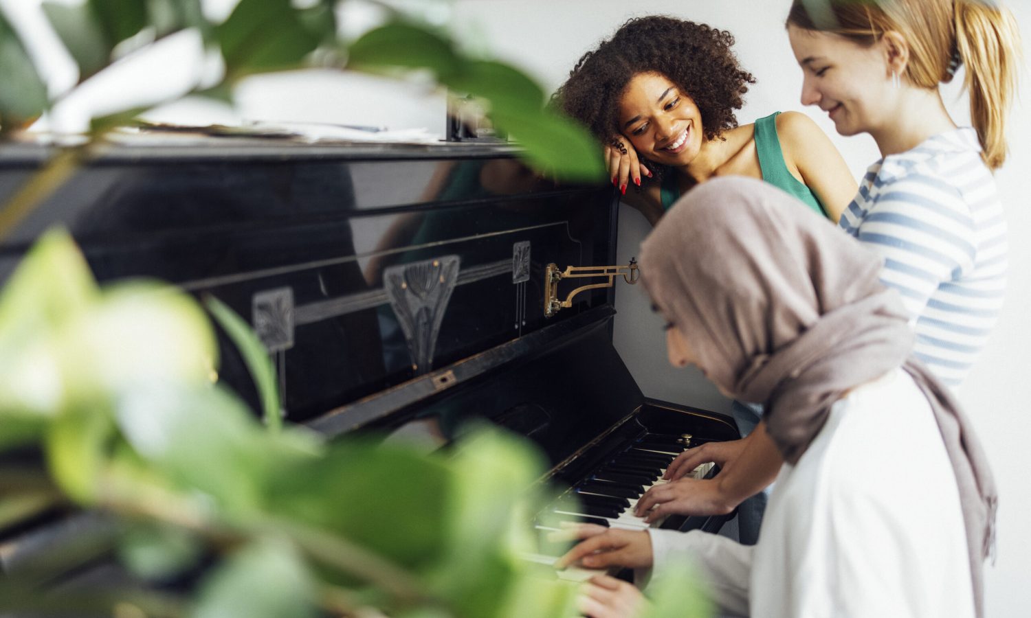 De jolies adolescentes souriantes jouent des duos sur le vieux piano. Des adolescents caucasiens, afro-américains et musulmans écoutent de la musique. 2 personnes jouent du piano et une 1 personne regarde et écoute le piano